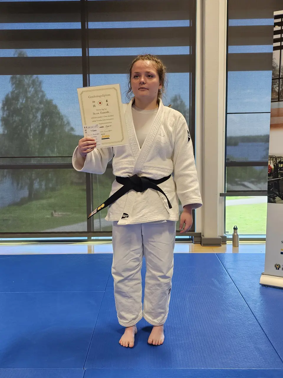 Felicia visar upp sitt diplom efter genomförd och godkänd gradering till svart bälte